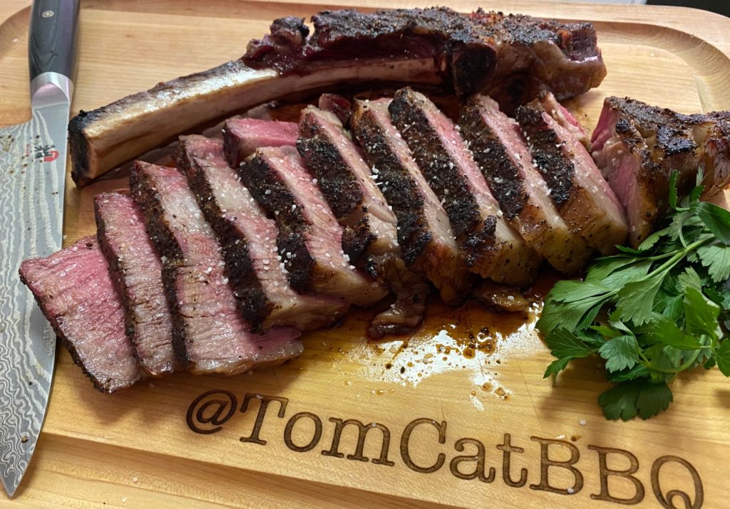 sliced ribeye steak on a cutting board with a knife and parsley